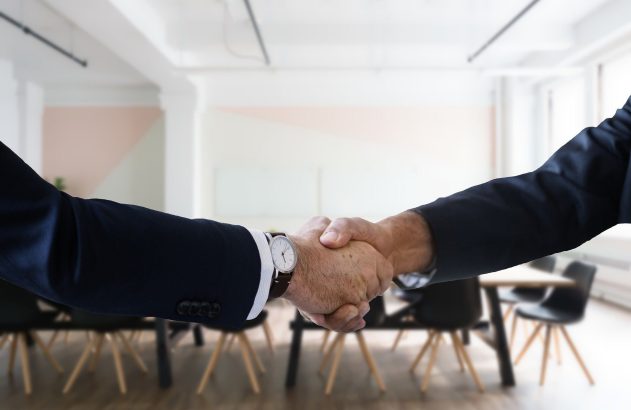 Duas pessoas de terno apertam as mãos em um escritório.