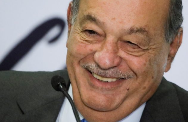 Homem mais velho com bigode, de terno, sorri amplamente com os olhos cerrados, perto de um microfone.