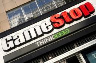 Letreiro da GameStop com letras brancas e vermelhas, e "THINKGEEK" em verde, na fachada de um edifício.