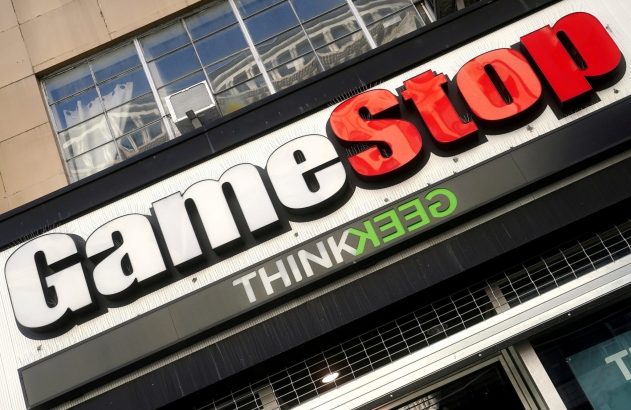 Letreiro da GameStop com letras brancas e vermelhas, e "THINKGEEK" em verde, na fachada de um edifício.