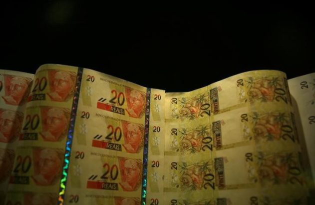 Cédulas de 20 reais do Brasil em folha, com faixa holográfica visível.