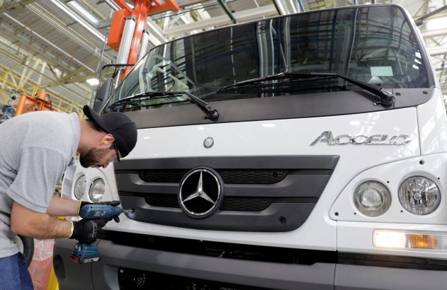 Operário com furadeira elétrica trabalhando na montagem de um caminhão Mercedes-Benz Accelo branco em fábrica.