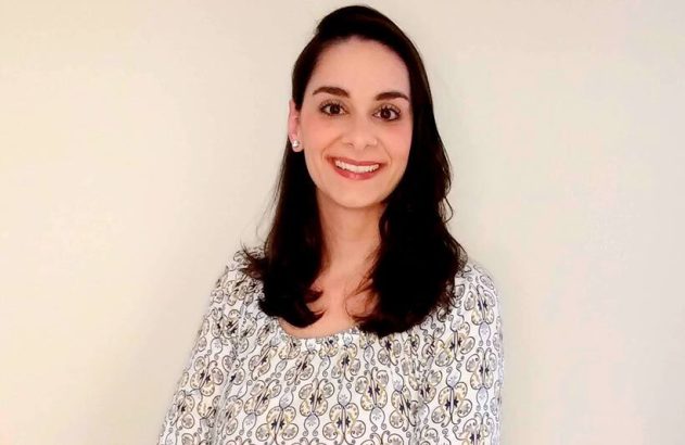 Mulher de cabelos escuros e blusa estampada sorri para a câmera.