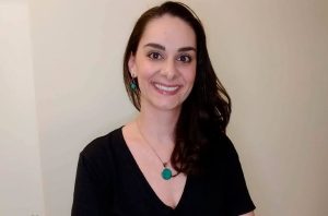 Mulher sorridente de cabelo escuro e joias turquesa, olhando para a câmera.