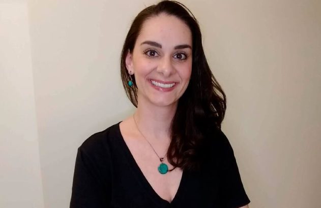 Mulher sorridente de cabelo escuro e joias turquesa, olhando para a câmera.