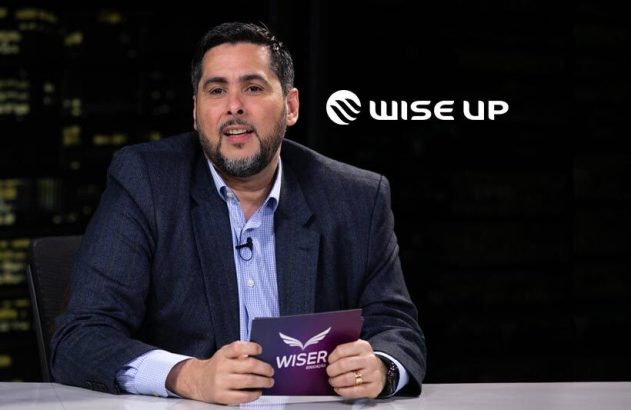Homem apresentador em estúdio escuro, com logo Wise Up ao fundo, fala segurando um objeto na mão.
