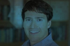 Retrato de homem jovem sorrindo, olhando para frente. Imagem com tonalidade azul-esverdeada e efeito de blocos pixelados.