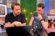 Dois homens interagem com um laptop. Um aponta para a tela, o outro observa.