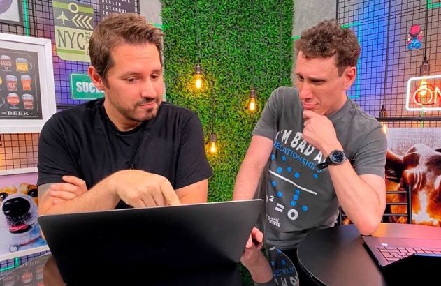 Dois homens interagem com um laptop. Um aponta para a tela, o outro observa.