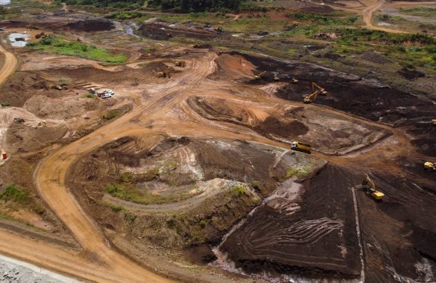 Vista aérea de mineração a céu aberto com escavadeiras, caminhões e extensas áreas de terra movimentada.