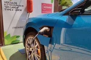 Carro elétrico azul carregando em estação Incharge. Placa informa "VEÍCULOS ELÉTRICOS EM CARGA, TYPE 2 - 22KW".
