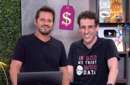 Dois homens sorrindo em um estúdio com uma etiqueta de preço e decorações temáticas.