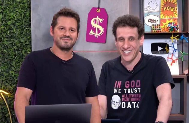 Dois homens sorrindo em um estúdio com uma etiqueta de preço e decorações temáticas.