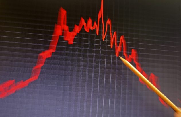 Uma tela exibe um gráfico de linha vermelho em forte declínio, com uma caneta amarela apontando para o ponto mais baixo.