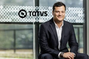 Homem sorridente de terno. Logo TOTVS em janela ao fundo.