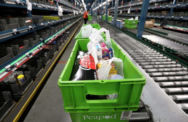 Cesto verde Peapod com mantimentos (refrigerante, cereais) em esteira transportadora de armazém.