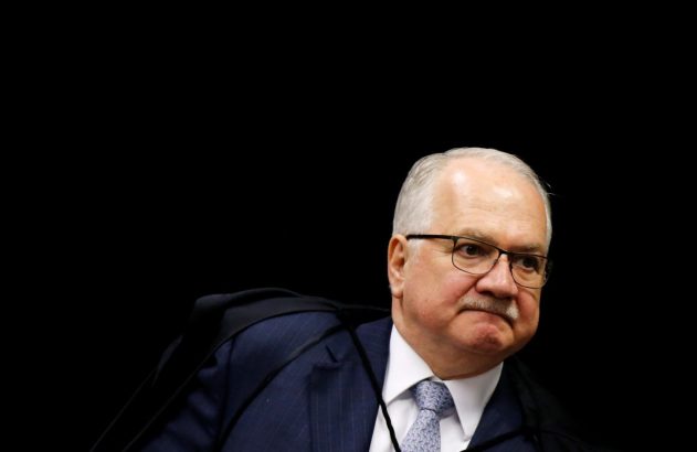 Homem de óculos, bigode e terno com toga preta, com expressão séria, olhando para a direita.