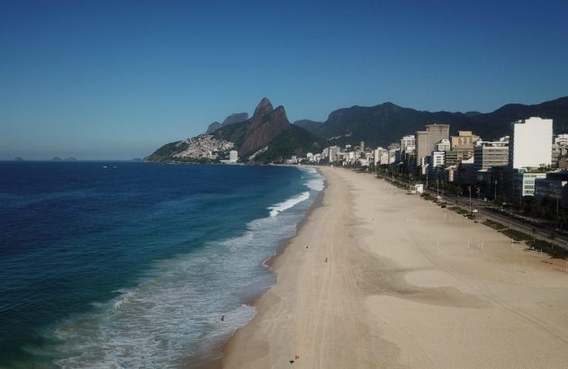 Praia de Ipanema, Rio de Janeiro: longa faixa de areia com pessoas, mar azul, edifícios e montanhas.