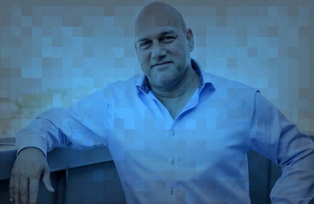 Homem calvo de camisa azul clara, apoiado e olhando para o observador.