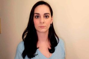 Retrato de mulher com cabelos escuros e olhar intenso, vestindo blusa azul.