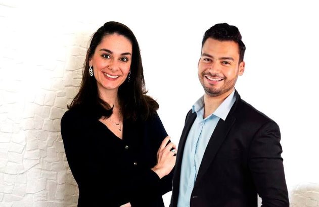 Homem e mulher sorrindo para a câmera, em trajes profissionais, fundo branco.