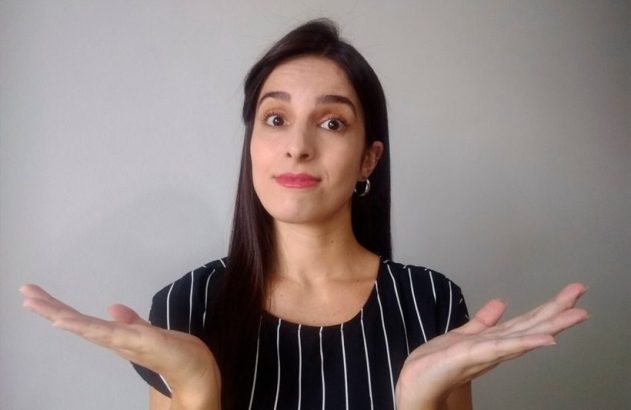 Mulher com expressão de dúvida e mãos abertas, em fundo cinza.