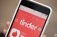 Mão segurando um iPhone com a página do aplicativo Tinder aberta na loja de apps.