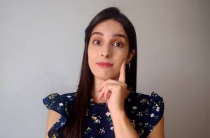 Mulher pensativa com a mão no queixo, olhando para a câmera.