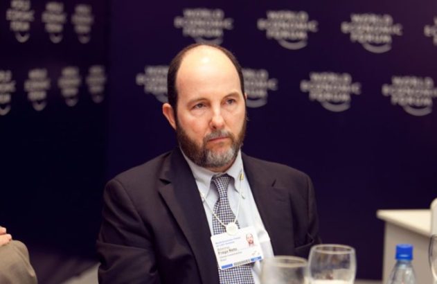 Homem com barba e crachá do Fórum Econômico Mundial sentado em evento.