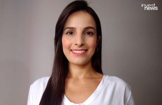 Mulher jovem com cabelo escuro e liso, sorrindo e olhando para a câmera, vestindo blusa branca.