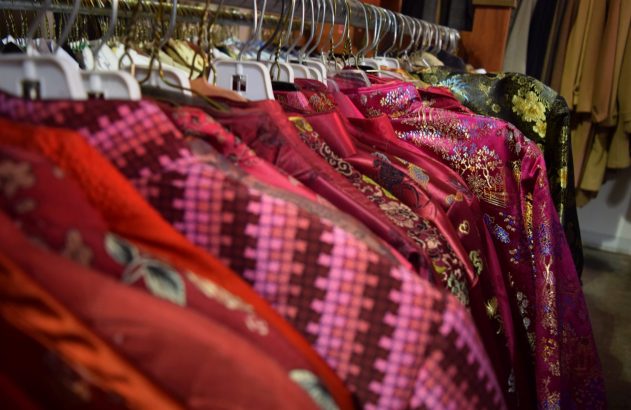 Fileira de roupas de seda coloridas com padrões orientais penduradas em cabides, em tons de vermelho e rosa.