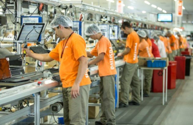 Trabalhadores da Positivo em linha de montagem de eletrônicos, manuseando equipamentos e usando toucas.