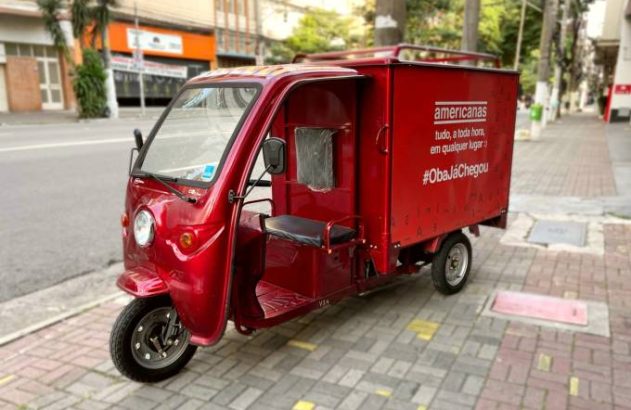 Triciclo de entregas vermelho da Americanas estacionado na calçada.