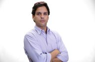 Homem em camisa lilás, braços cruzados, com olhar direto para a câmera em fundo branco.