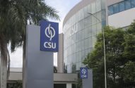 Prédio corporativo moderno da CSU com fachada de vidro. Dois letreiros azuis com o logo 'CSU' se destacam entre palmeiras.