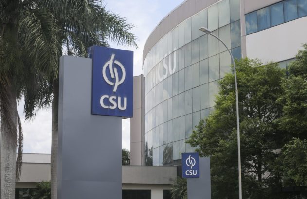 Prédio corporativo moderno da CSU com fachada de vidro. Dois letreiros azuis com o logo 'CSU' se destacam entre palmeiras.