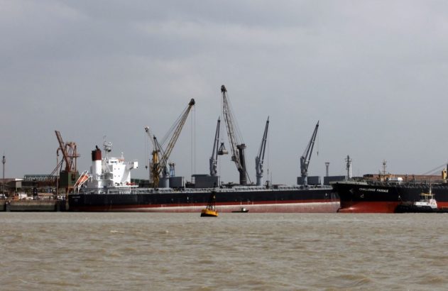 Dois navios de carga atracados em porto, com silos e guindastes.