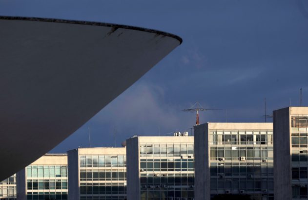 Curva de edifício branco em primeiro plano, prédios modernos de escritórios com janelas e antenas sob céu escuro.