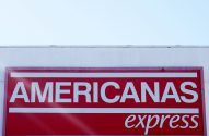 Letreiro vermelho "AMERICANAS express" em prédio branco sob céu azul.
