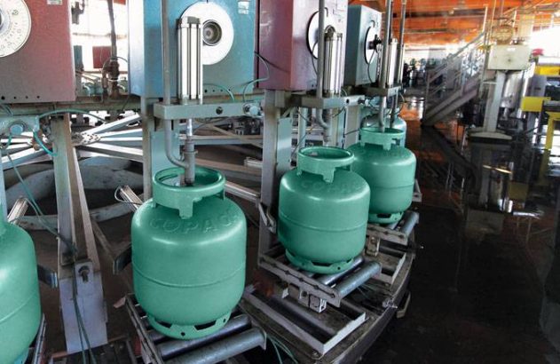 Botijões de gás verdes sendo envasados por máquinas numa linha de produção industrial.