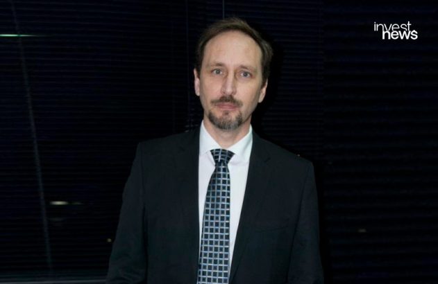 Homem de terno e gravata, olhando para a câmera, com fundo escuro.