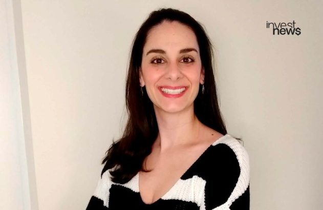 Mulher de cabelo escuro, sorrindo, em suéter preto e branco. Logo 'invest news' no canto superior direito.