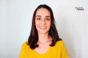 Mulher sorridente de cabelo escuro e blusa amarela. Fundo texturizado claro com logo Invest News.