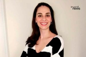 Retrato de mulher sorrindo, com suéter preto e branco. Logo "invest news" no canto superior direito.
