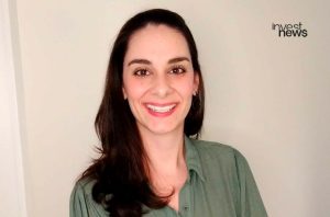Retrato de mulher sorrindo, cabelo escuro, camisa verde. Logo 'invest news' visível.