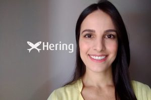 Mulher sorridente com o logo da Hering (dois peixes) ao fundo.