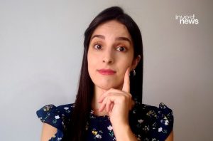 Mulher com olhos arregalados, dedo no rosto, em pose pensativa ou questionadora.