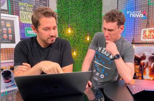 Dois homens olhando para um laptop em uma mesa; um aponta para a tela, o outro observa pensativo.