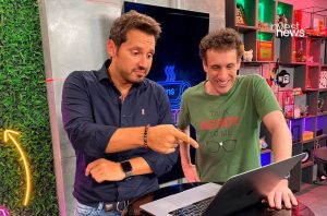 Dois homens interagem com um laptop. Um aponta para a tela, o outro sorri.