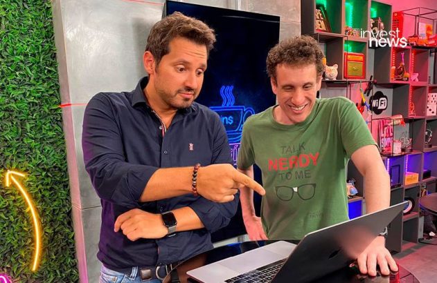 Dois homens interagem com um laptop. Um aponta para a tela, o outro sorri.